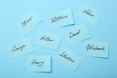 Photo of Choosing baby name. Paper stickers with different names on light blue background, flat lay