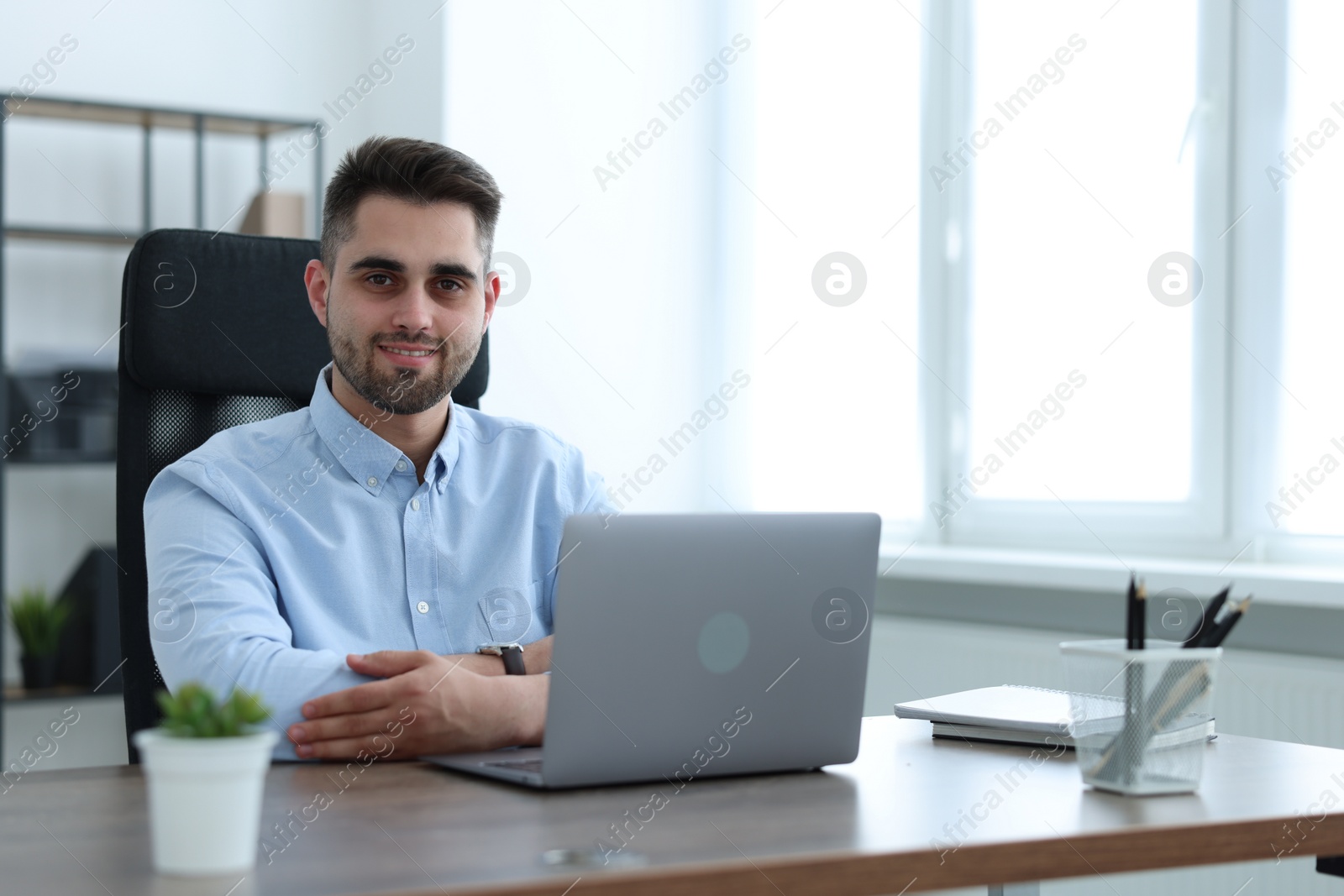 Photo of Happy young programmer working with laptop in office