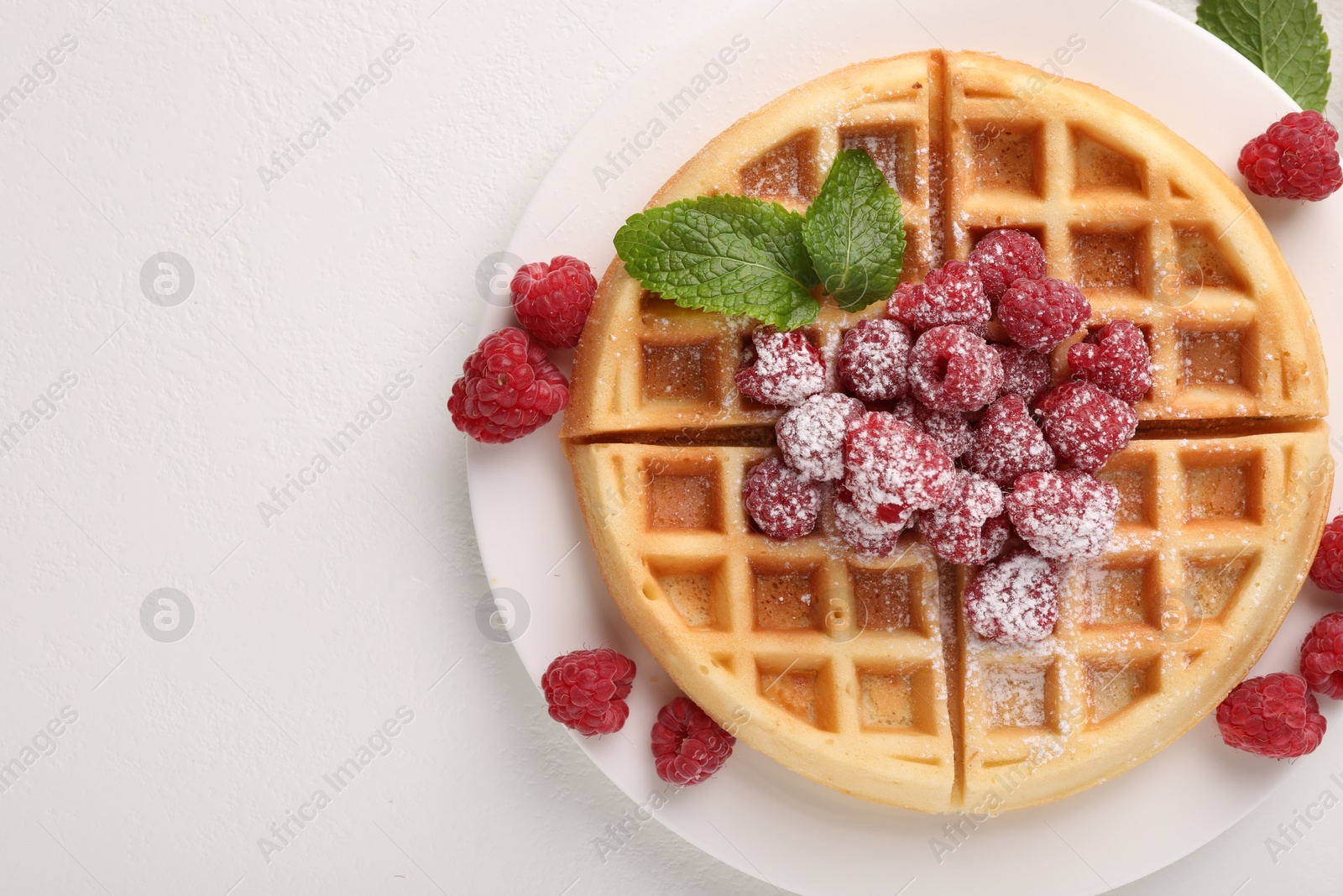 Photo of Tasty Belgian waffle with fresh raspberries, powdered sugar and mint on white table, top view. Space for text