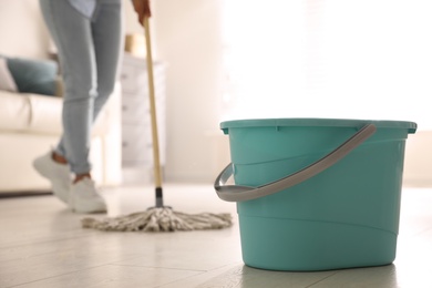 Photo of Plastic bucket and woman mopping floor in living room, closeup. Cleaning supplies