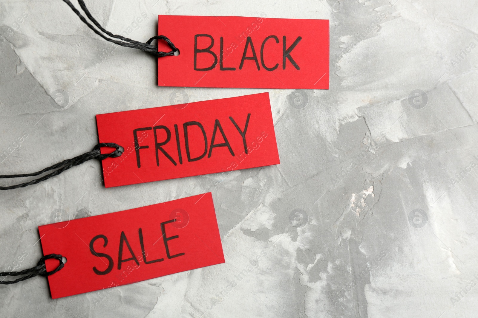 Photo of Red tags with words BLACK FRIDAY SALE on light grey stone background, flat lay. Space for text