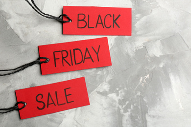 Photo of Red tags with words BLACK FRIDAY SALE on light grey stone background, flat lay. Space for text