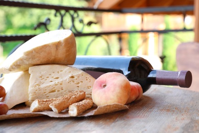 Photo of Delicious cheese, ripe peaches and bottle of wine on wooden table