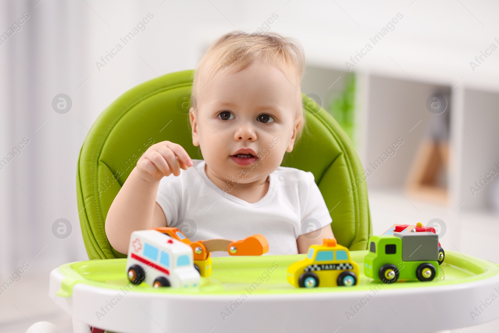 Photo of Children toys. Cute little boy playing with toy cars in high chair at home