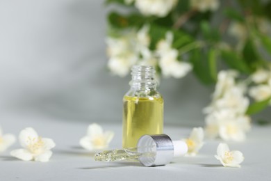 Photo of Essential oil in bottle, beautiful jasmine flowers and pipette on grey background, closeup