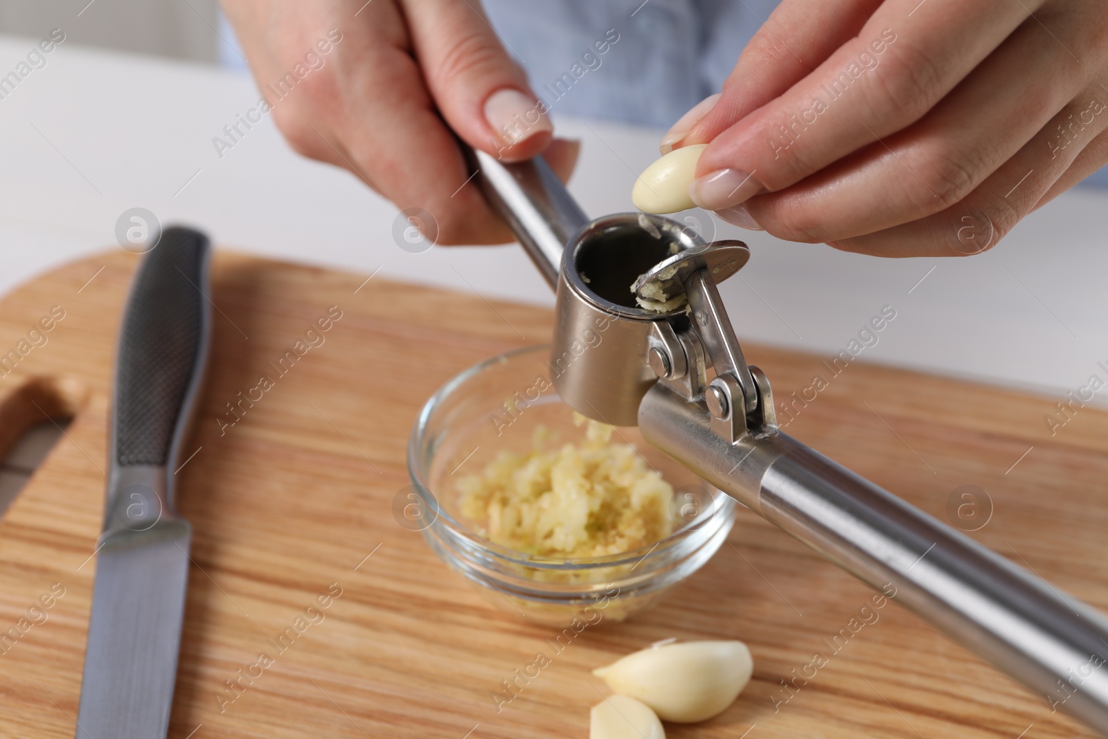 Photo of Woman squeezing garlic with press at wooden table, closeup