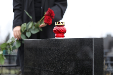 Photo of Woman with red roses outdoors, focus on candle. Funeral ceremony