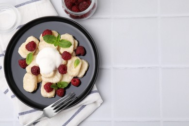 Photo of Plate of tasty lazy dumplings with raspberries, sour cream and mint leaves on white tiled table, flat lay. Space for text