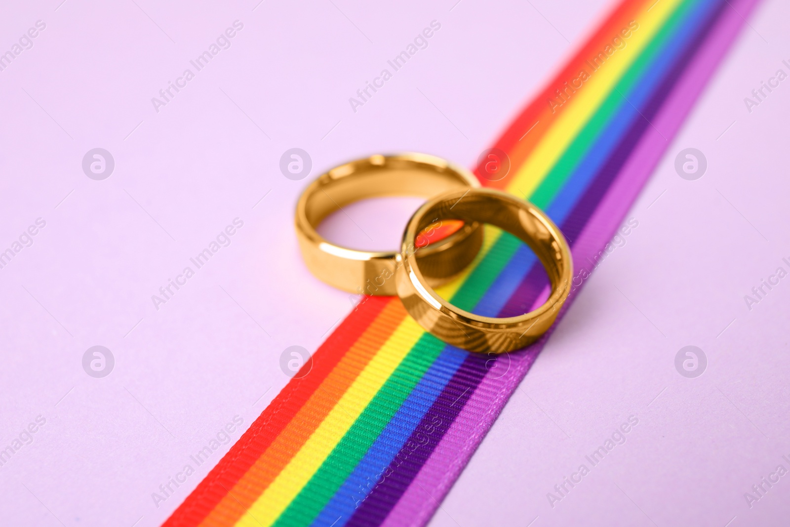 Photo of Wedding rings and rainbow ribbon on color background. Gay symbol