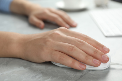Photo of Woman using wired computer mouse at light grey marble table, closeup