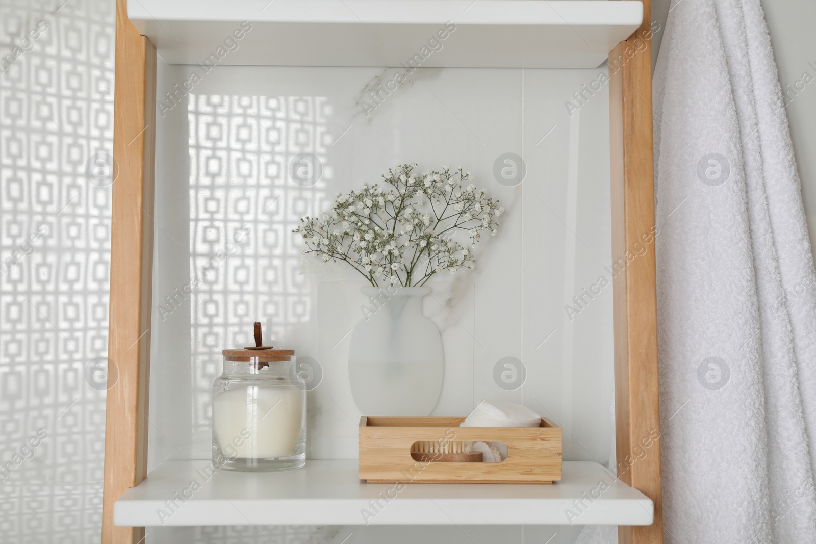 Photo of Silicone vase with flowers on white marble wall and shelving unit in stylish bathroom