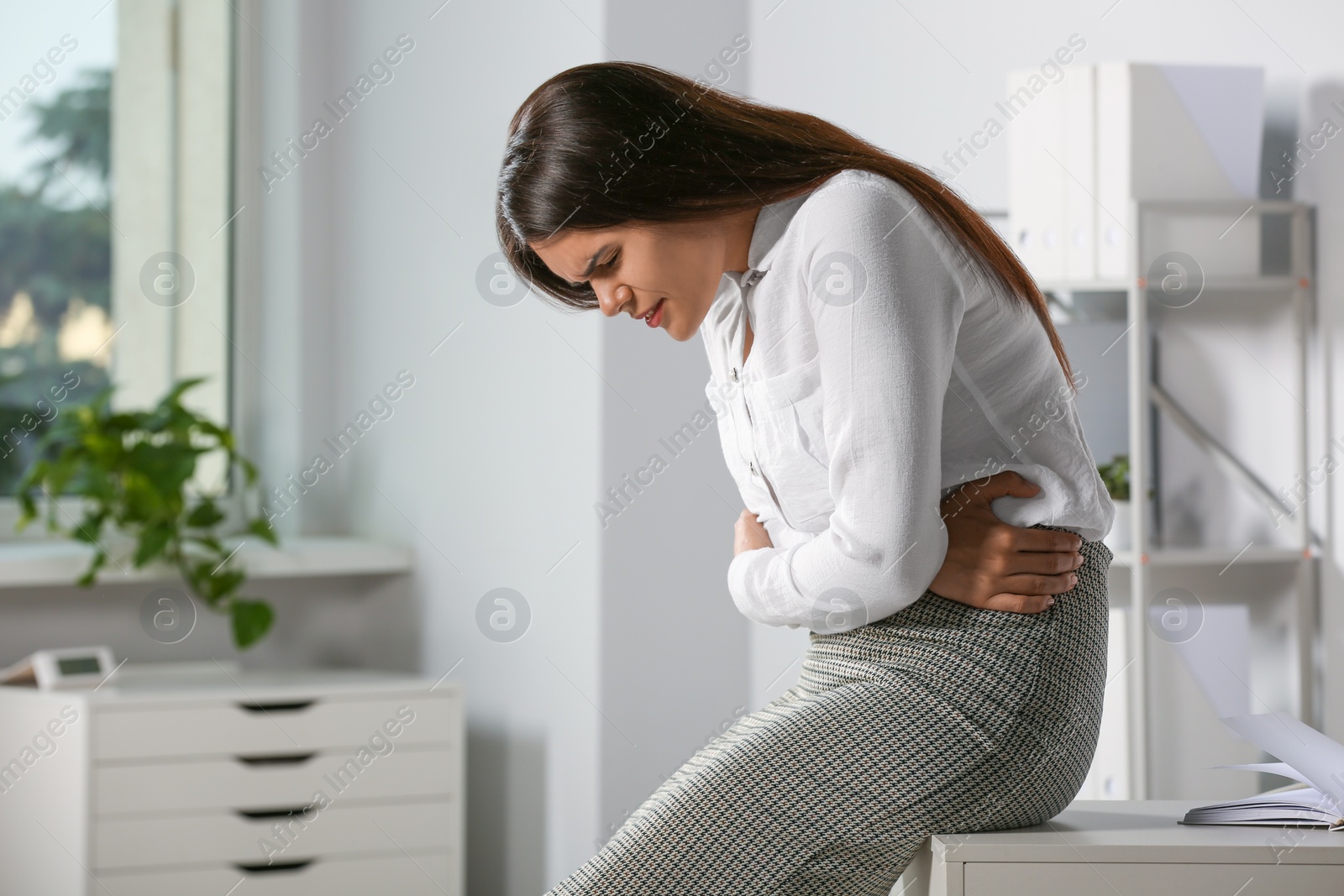 Photo of Young woman suffering from menstrual pain in office