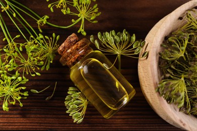 Bottle of essential oil and fresh dill on wooden table, flat lay