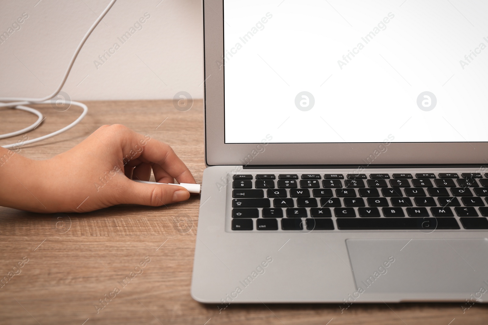Photo of Woman connecting charge cable to laptop on wooden table, closeup. Space for text