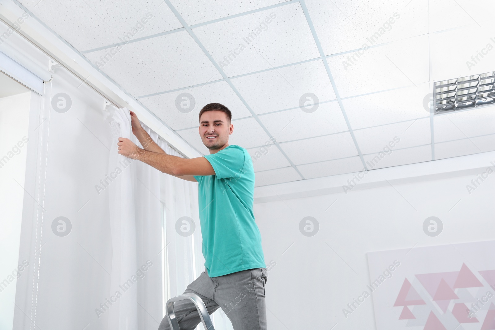 Photo of Man hanging window curtain indoors. Interior decor element