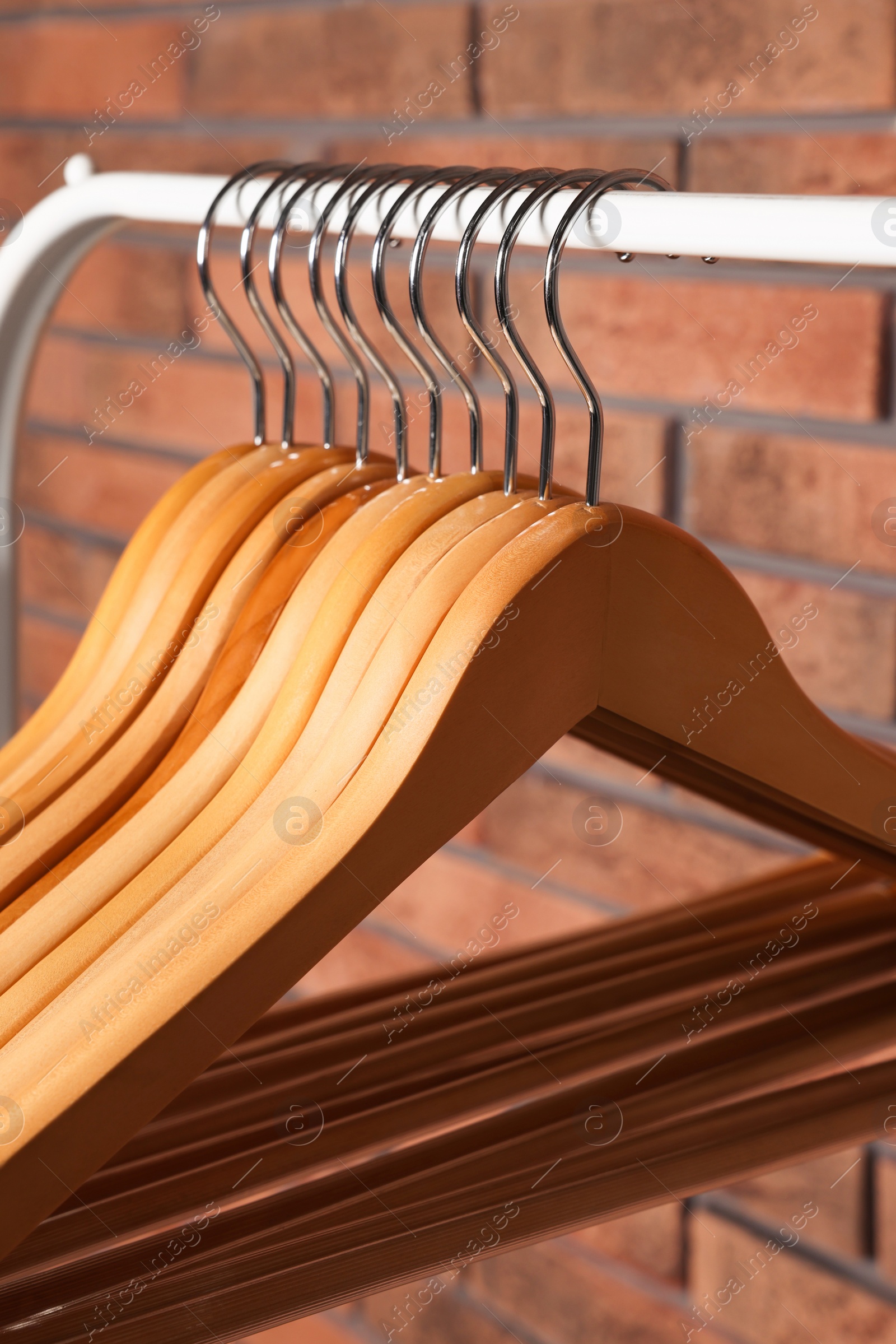 Photo of Wooden clothes hangers on rack near red brick wall, closeup