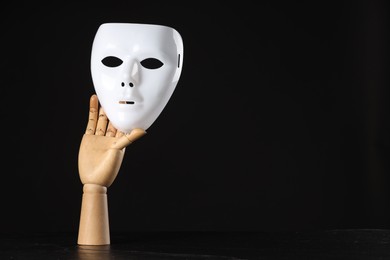 Wooden mannequin hand holding plastic mask on black background, space for text. Theatrical performance