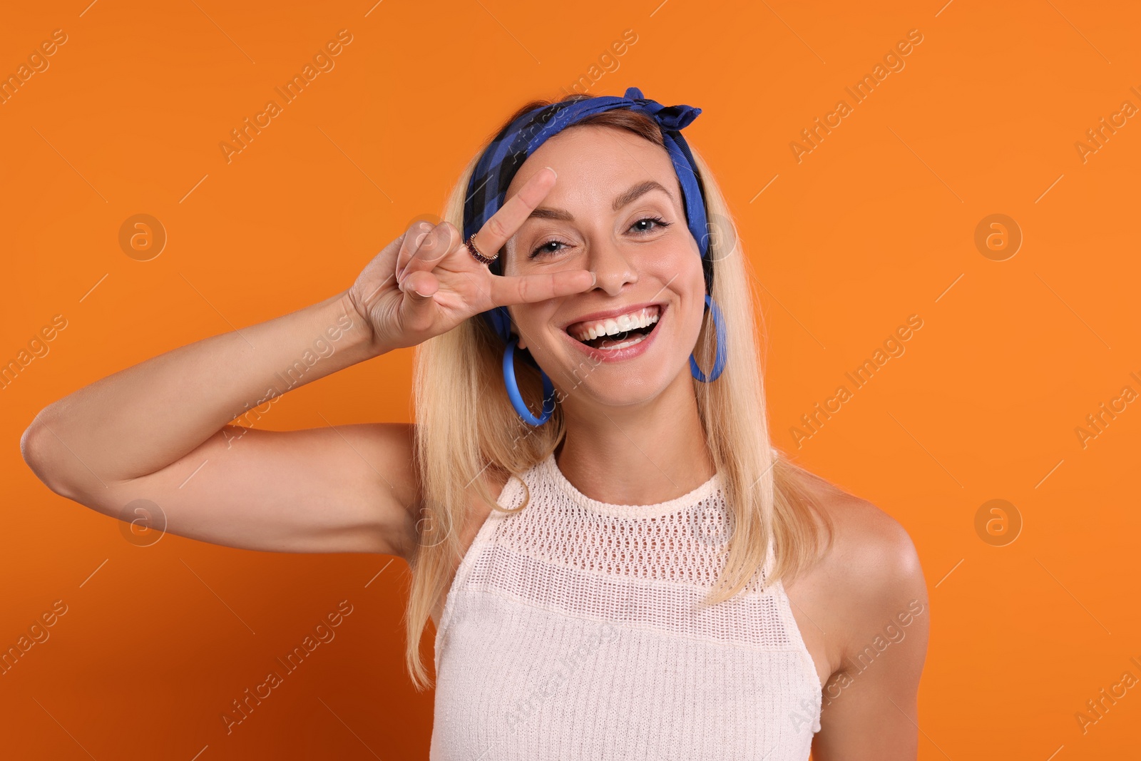 Photo of Portrait of smiling hippie woman showing peace sign on orange background
