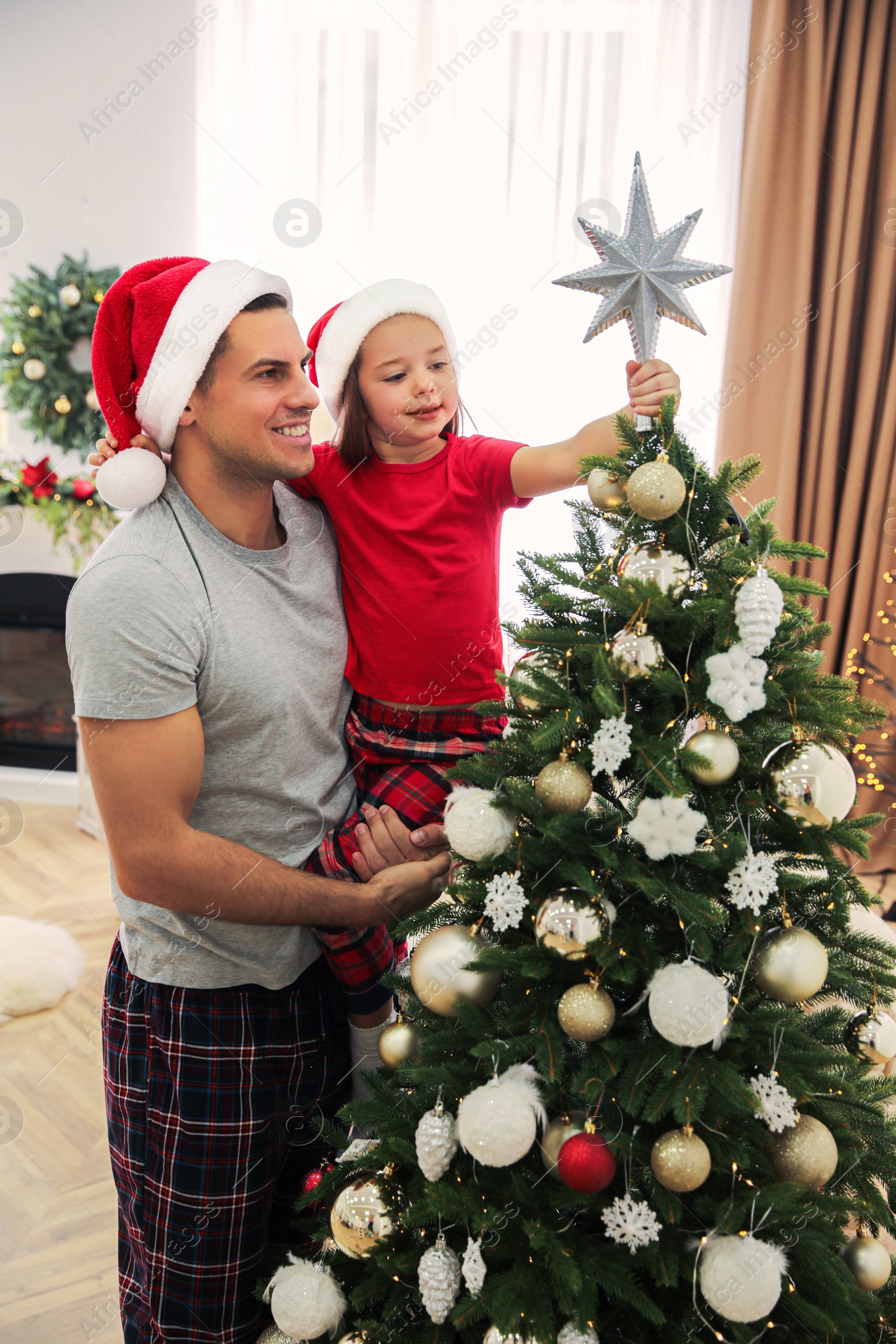 Photo of Father and little daughter decorating Christmas tree with star topper indoors