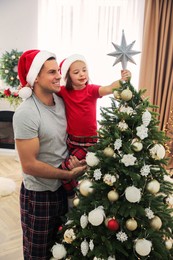 Father and little daughter decorating Christmas tree with star topper indoors