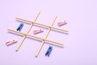 Tic tac toe game made with clothespins on violet background, space for text