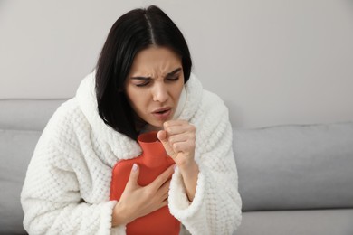 Photo of Ill woman with hot water bottle coughing at home