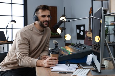 Photo of Man with cup of coffee working as radio host in modern studio