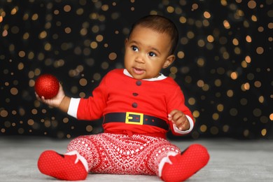 Cute little African American baby with Christmas ball and blurred lights on dark background