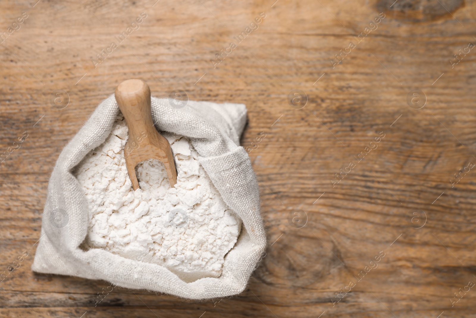 Photo of Wheat flour and scoop in sack bag on wooden table, top view. Space for text