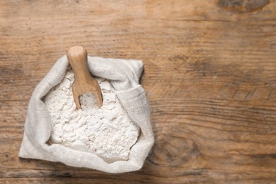 Photo of Wheat flour and scoop in sack bag on wooden table, top view. Space for text