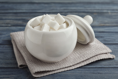 Refined sugar cubes in ceramic bowl on blue wooden table