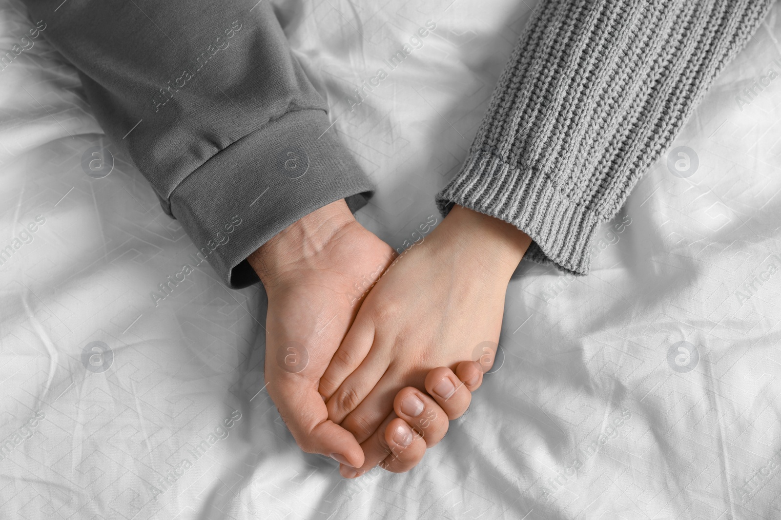 Photo of Couple holding hands on bed, top view