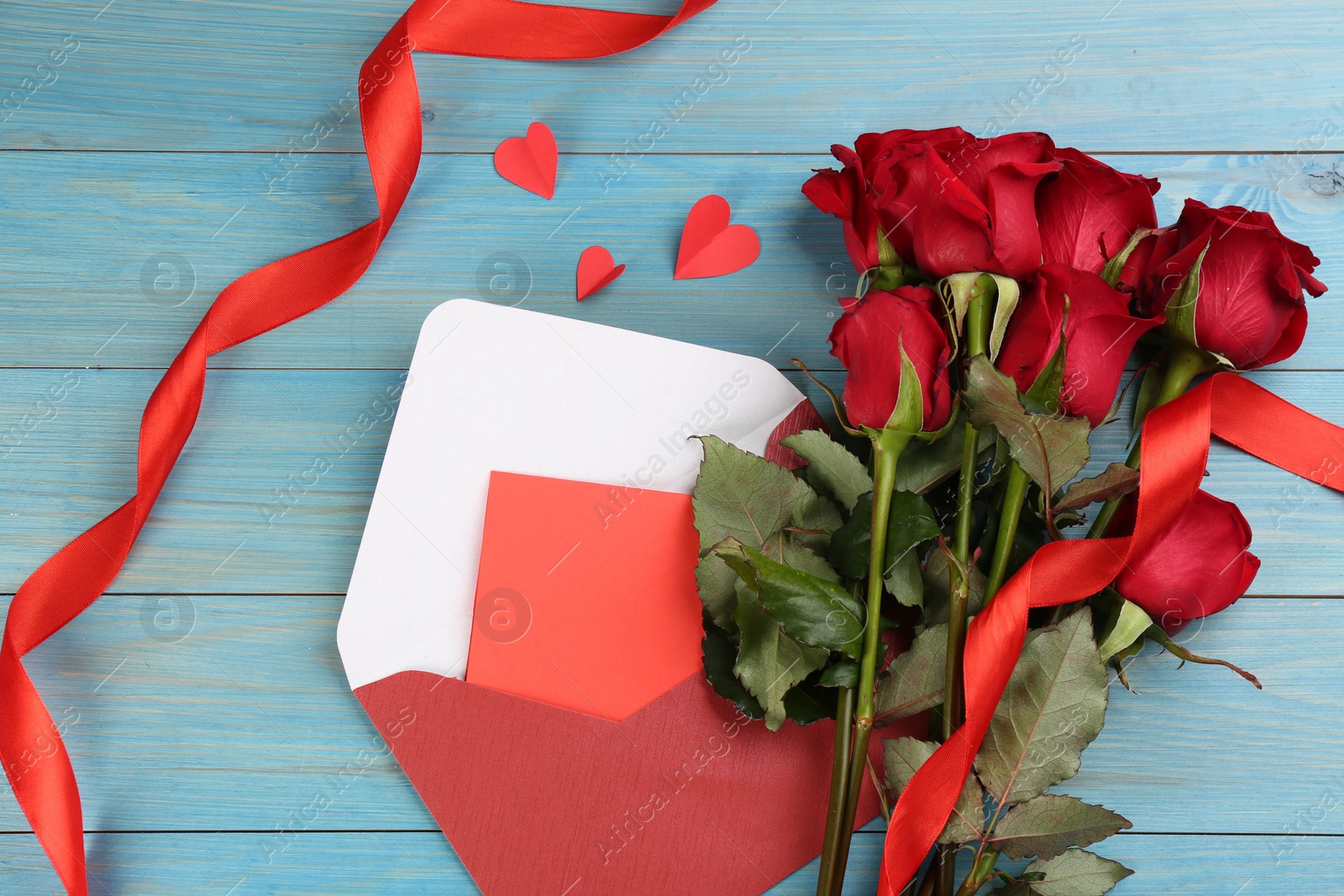Photo of Flat lay composition with beautiful red roses and love letter on light blue background. Valentine's Day celebration