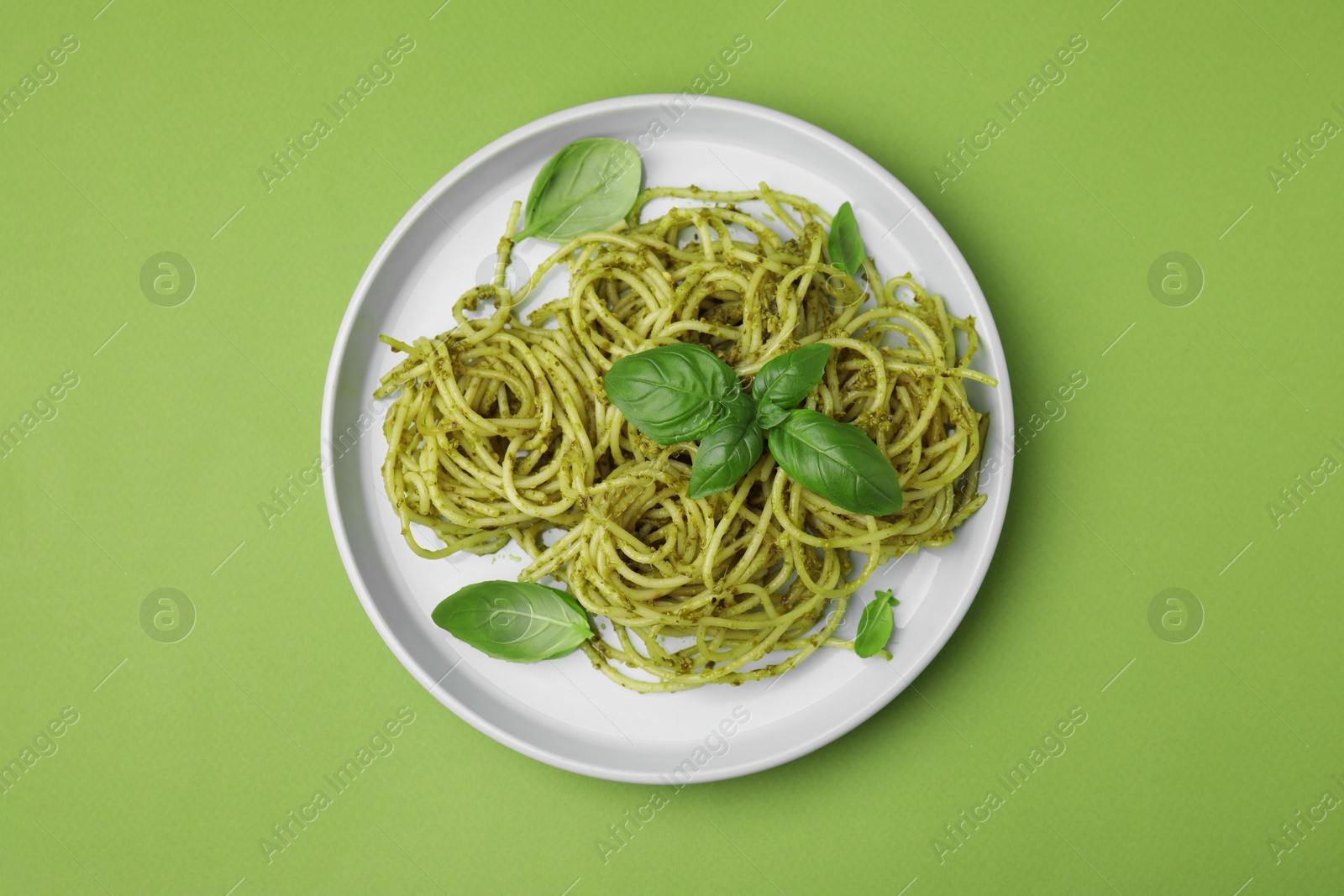 Photo of Delicious pasta with pesto sauce and basil on light green background, top view