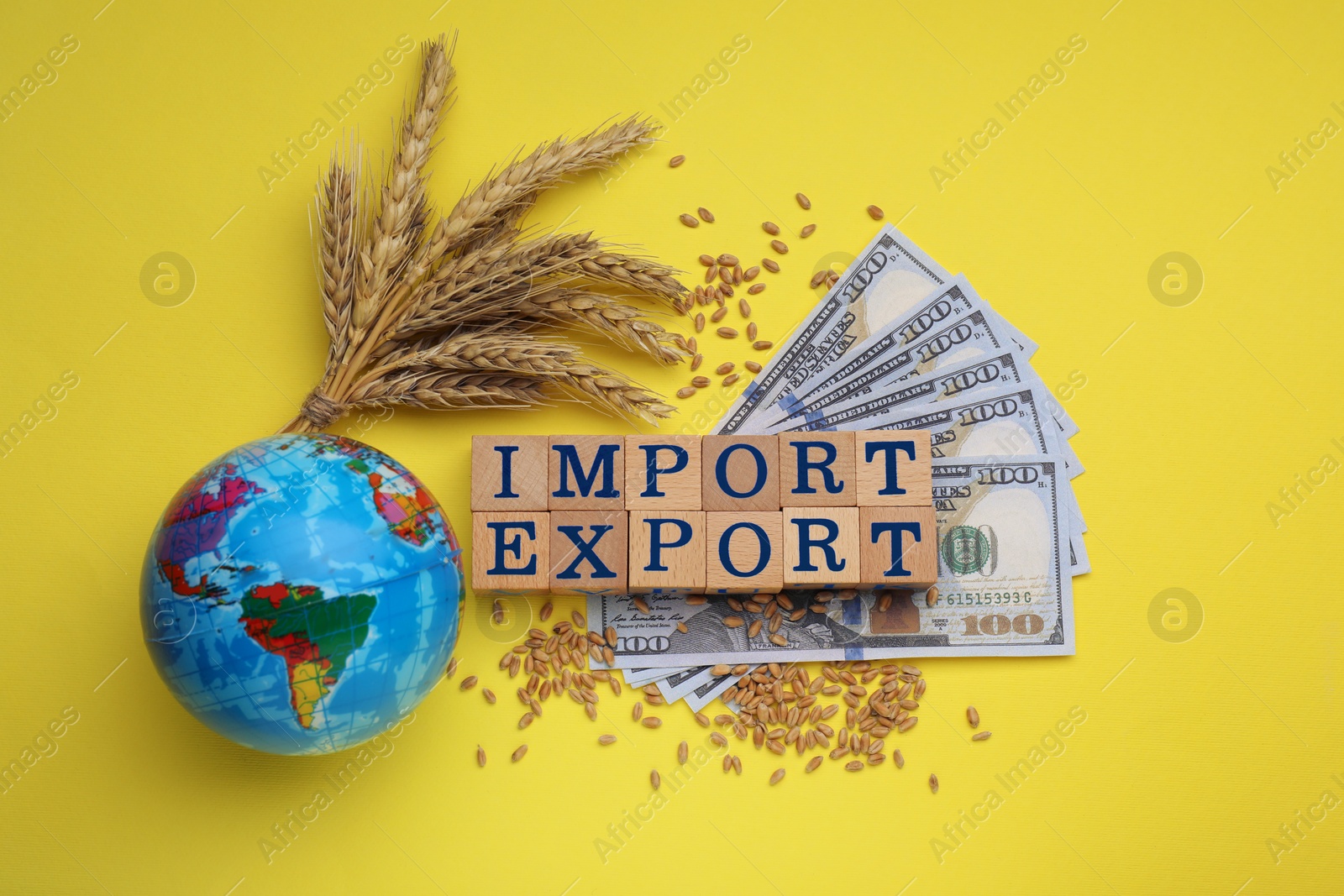 Photo of Words Import and Export made of wooden cubes, globe, ears of wheat and money on yellow background, flat lay