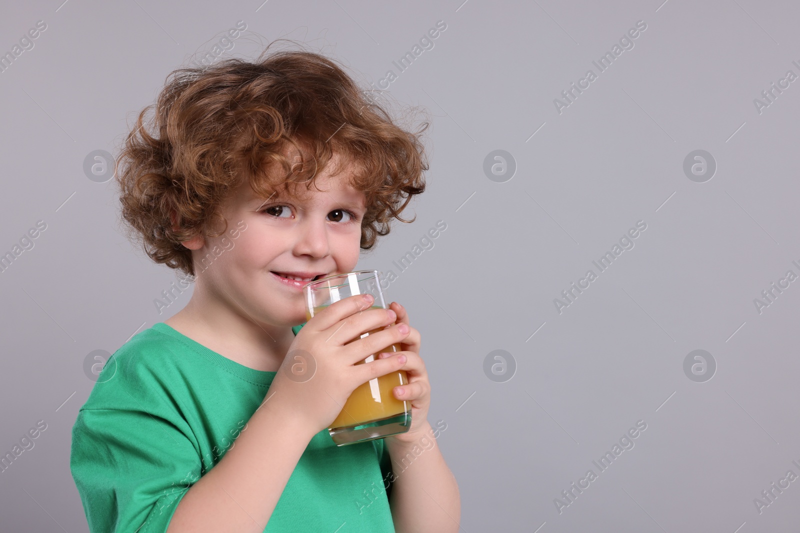 Photo of Cute little boy with glass of fresh juice on light gray background, space for text