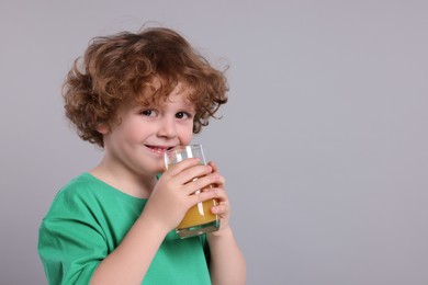 Cute little boy with glass of fresh juice on light gray background, space for text