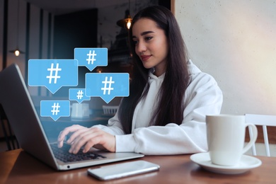 Young woman using modern laptop at table. Hashtag symbols over device