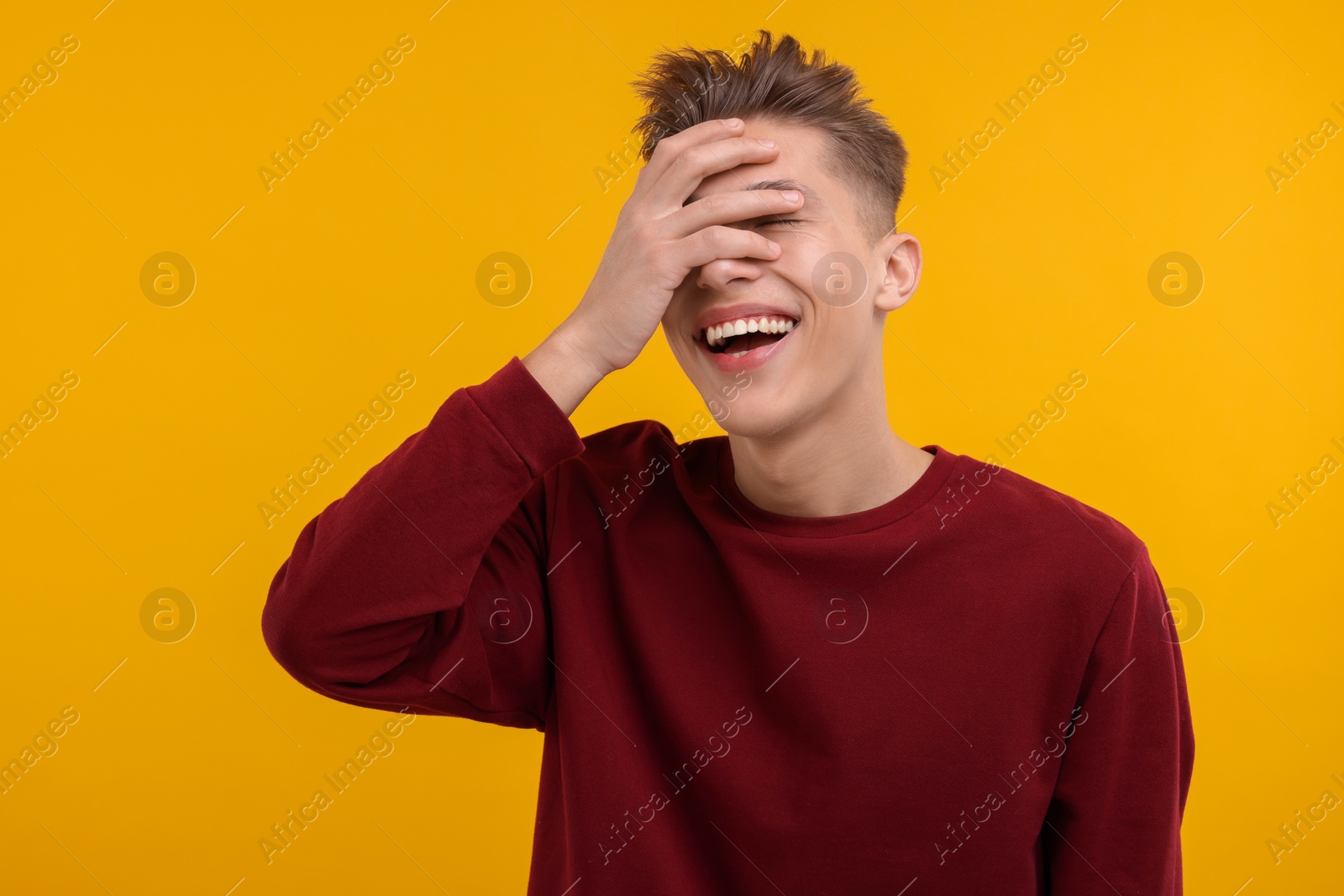 Photo of Young man covering eyes with hand and laughing on orange background