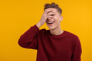 Young man covering eyes with hand and laughing on orange background