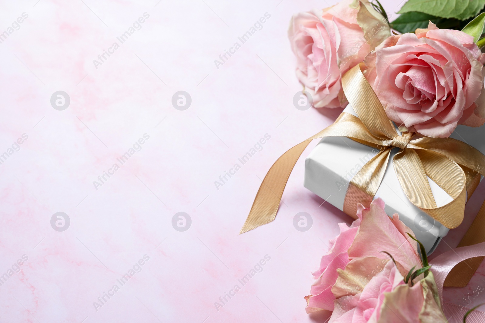 Photo of Beautiful roses and gift on light pink marble table, space for text. Happy birthday greetings