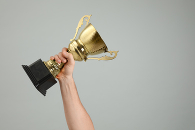 Photo of Man holding gold trophy cup on light grey background, closeup. Space for text