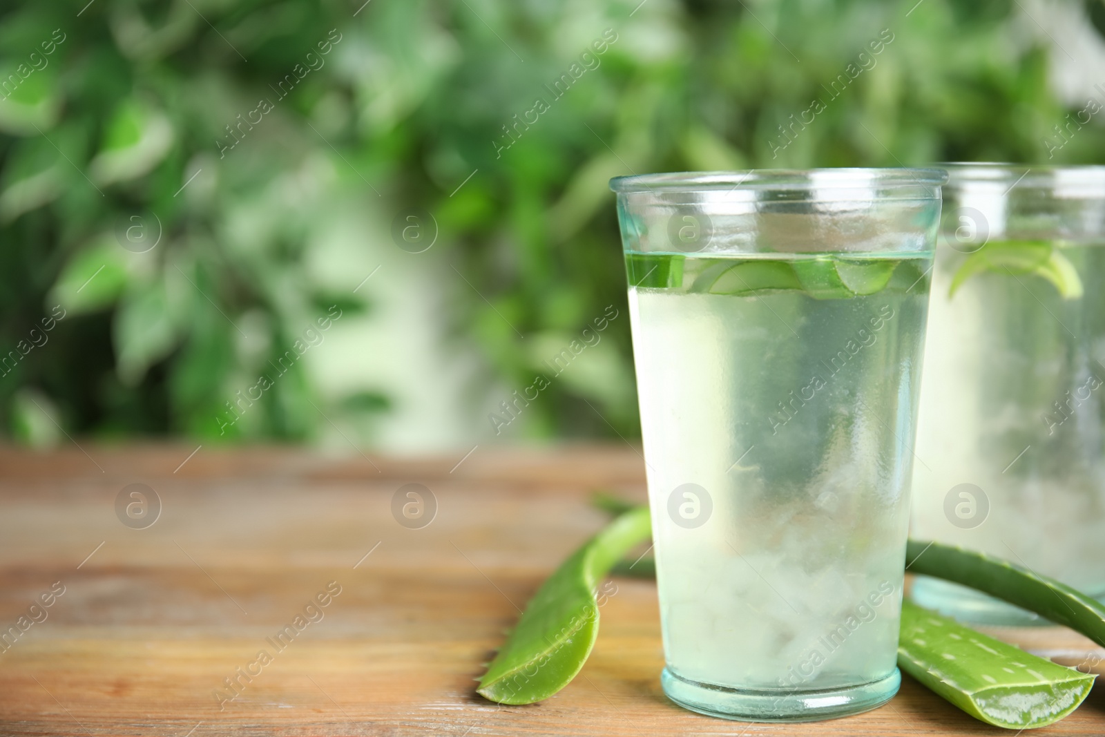 Photo of Fresh aloe drink in glasses and leaves on wooden table, space for text