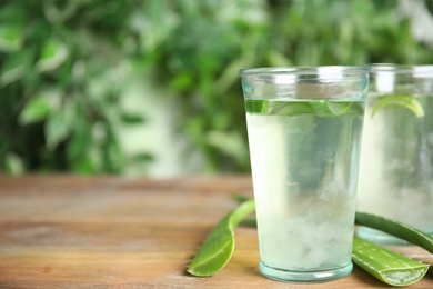 Photo of Fresh aloe drink in glasses and leaves on wooden table, space for text