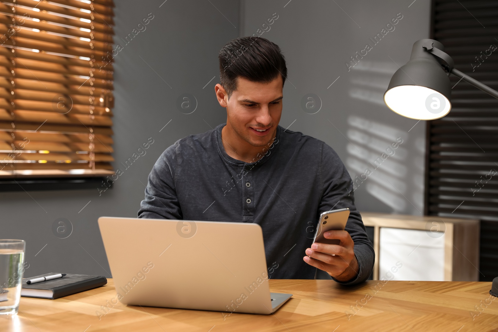 Photo of Man with modern smartphone and laptop at wooden table in office. Searching information