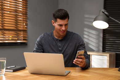 Photo of Man with modern smartphone and laptop at wooden table in office. Searching information