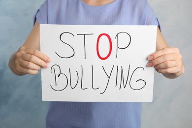 Photo of Woman holding paper sheet with phrase Stop Bullying on light blue background, closeup