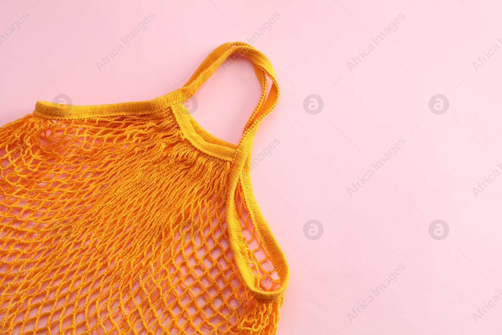 Photo of Orange string bag on pink background, top view. Space for text
