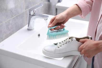 Photo of Woman washing stylish sneakers with brush in sink, closeup