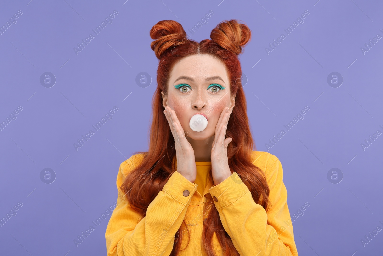 Photo of Portrait of surprised woman with bright makeup blowing bubble gum on violet background